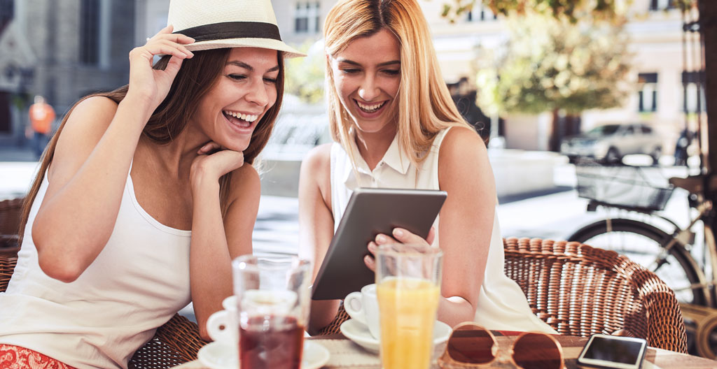 Groupe diversifié de jeunes étudiants en pleine conversation animée sur une terrasse de café ensoleillée, vus de profil et de dos